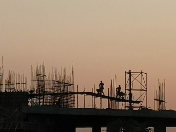 Eine Baustelle im indischen Mumbai mit zwei Arbeitern, die gegen den Abendhimmel deutlich zu erkennen sind.